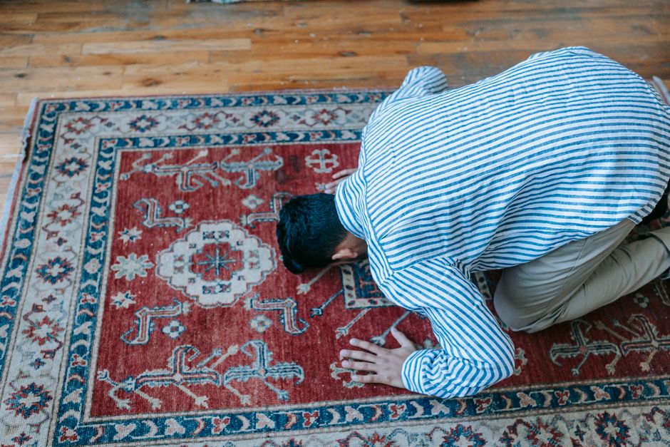 Close-up of an ornate, patterned area rug with a traditional design featuring orange, beige, and blue tones, placed on a wooden floor in a dining room. The rug appears clean and well-maintained, with 